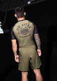 Male model wearing olive green and black BJJLIFESTYLE Jiu-Jitsu rashguard and fight shorts, back view.